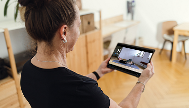 Eine Frau hält ein Tablet in der Hand, darauf zu sehen ein Ausschnitt der App für digitale Physiotherapie der eCovery GmbH