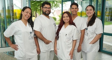 Symbolbild für das Unternehmen medicruiter: zu sehen sind 5 internationale Pflegefachkräfte im Eingangsbereich eines Krankenhauses  die in die Kamera lächeln
