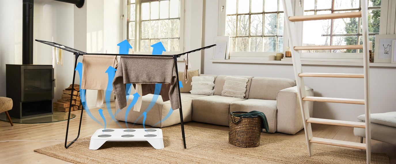 Der HEYDRY der TOSA home appliances GmbH steht unter einem Wäscheständer. Blaue Pfeile verdeutlichen die Wirkungsweise der Lüfter des Gerätes.