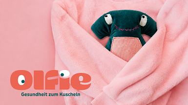 Das Kuscheltier Olfie ist leicht in eine Decke eingepackt.